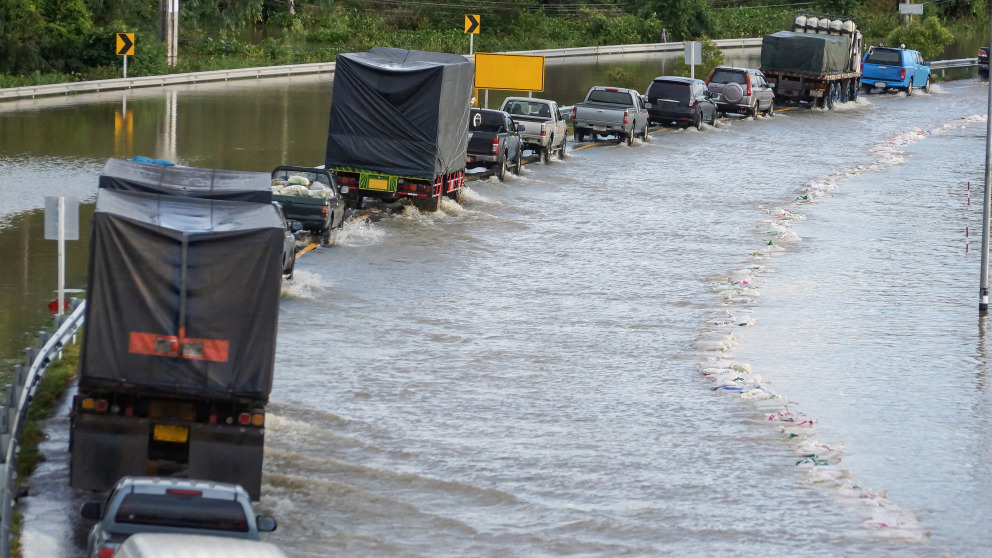 A row of cars, trucks, and lorries running through the flooded road.