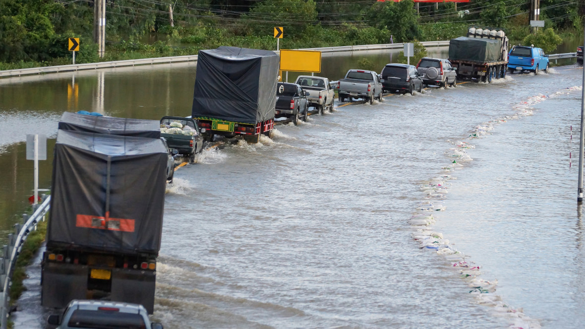 A row of cars, trucks, and lorries running through the flooded road.